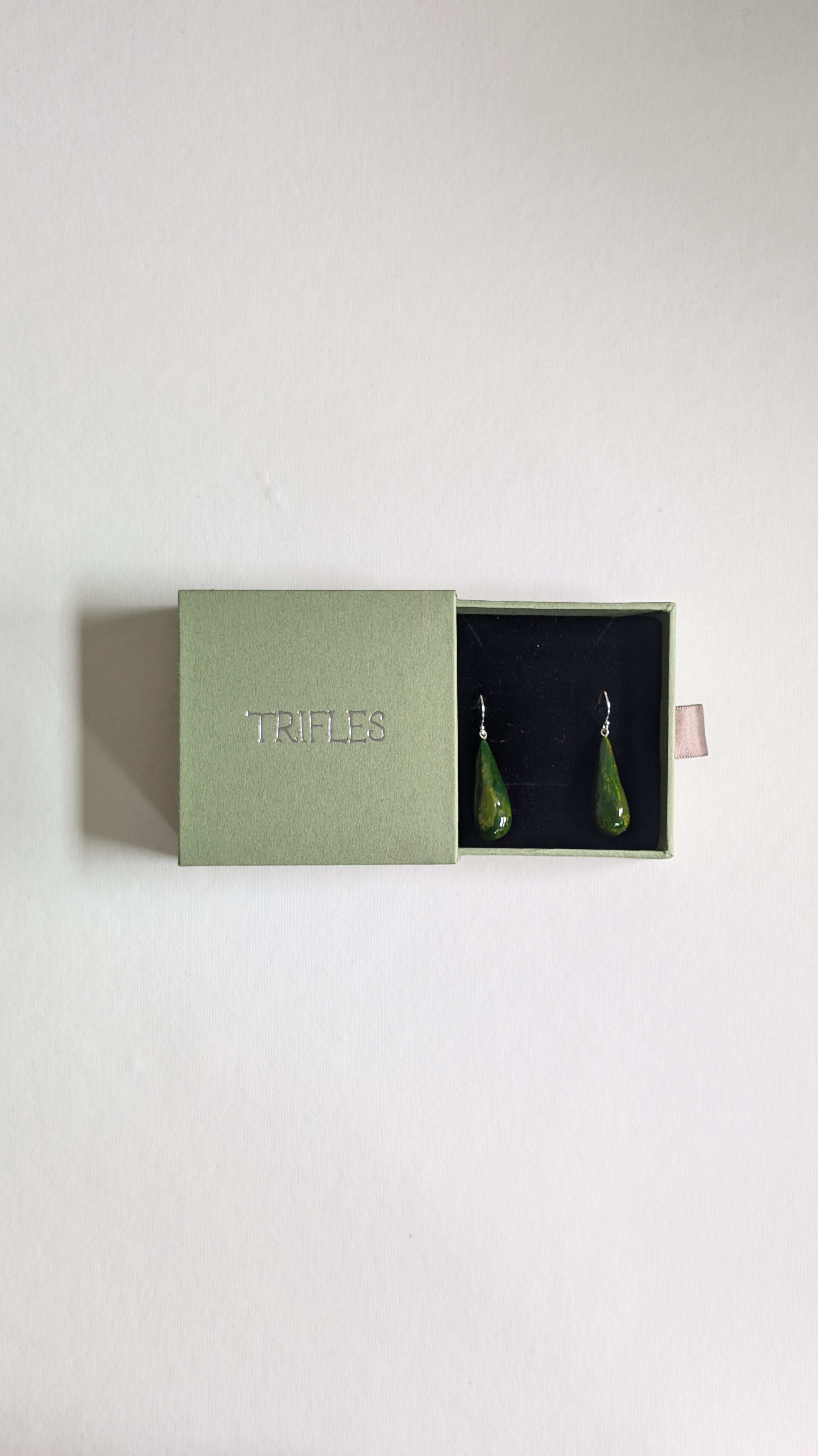Teardrop shaped handmade ceramic earrings painted in olive green and finished with sterling silver ear wires in Trifles gift box.