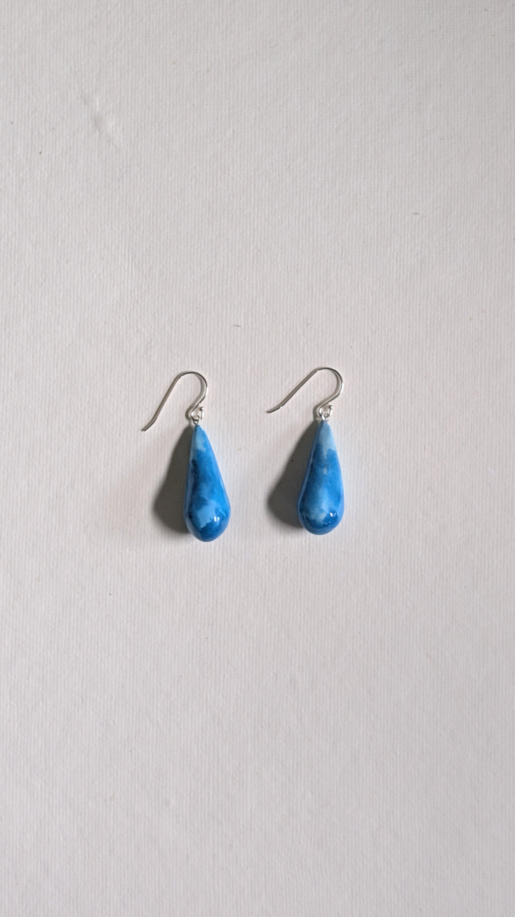 Teardrop shaped handmade ceramic earrings painted in sky blue and finished with sterling silver ear wires.