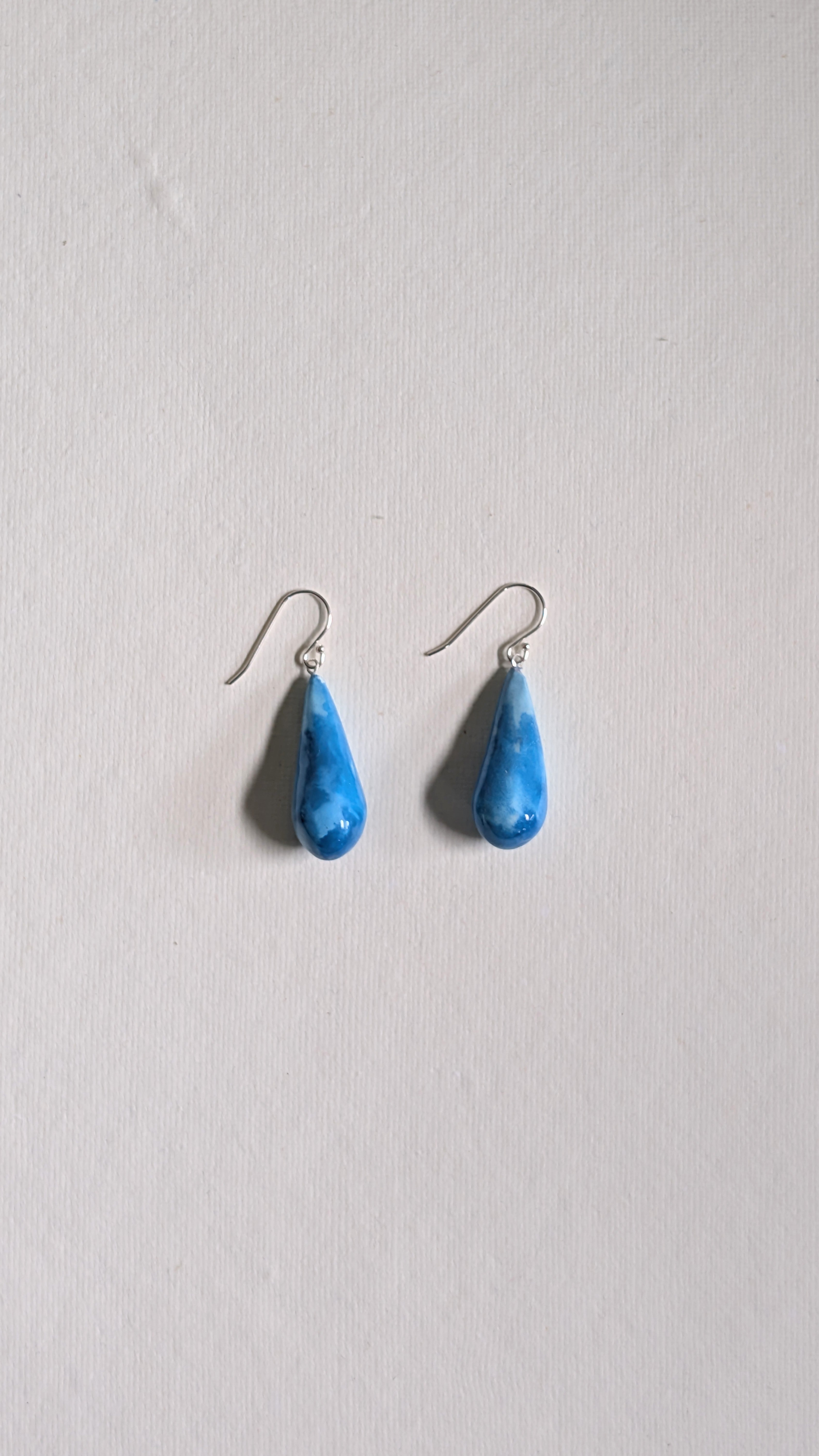 Teardrop shaped handmade ceramic earrings painted in sky blue and finished with sterling silver ear wires.
