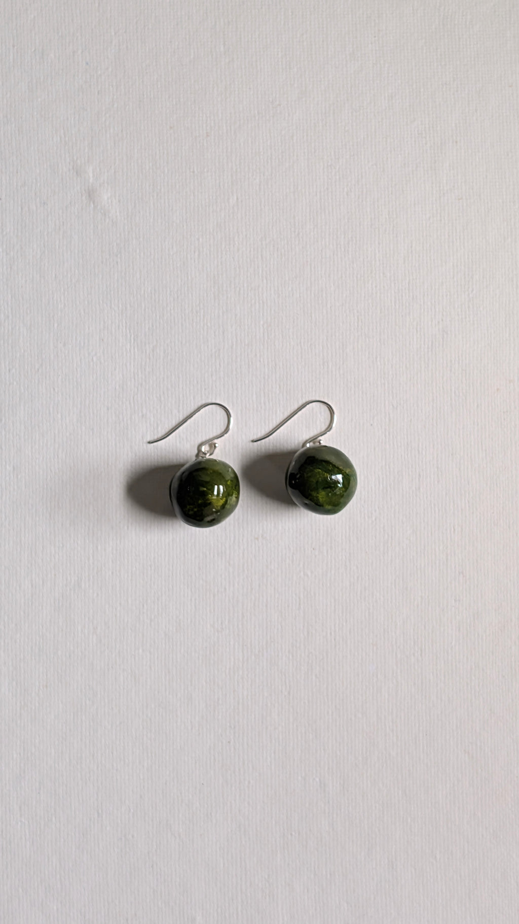 Handmade ceramic orb shaped earrings in olive green with sterling silver ear wires.