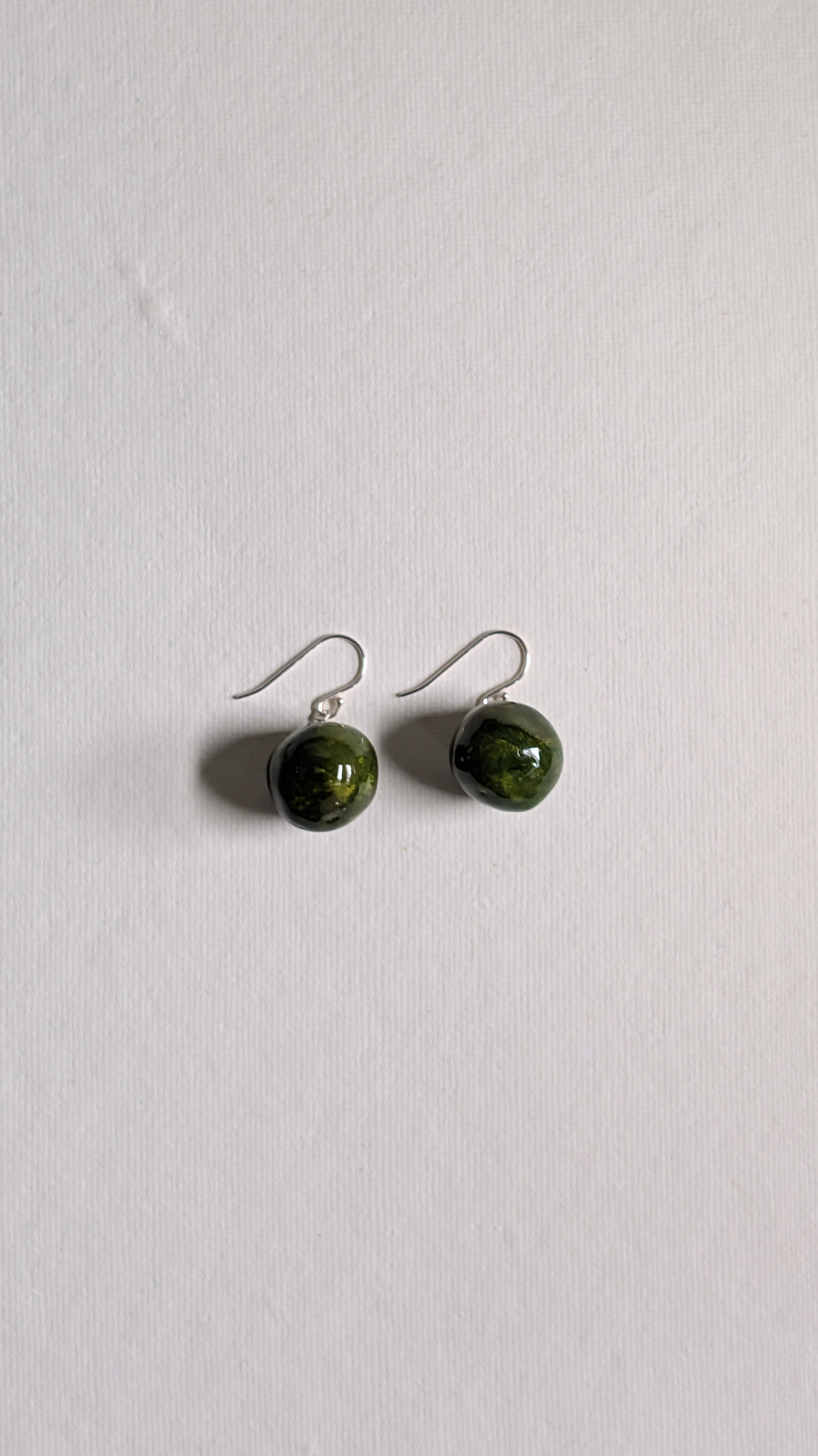 Handmade ceramic orb shaped earrings in olive green with sterling silver ear wires.