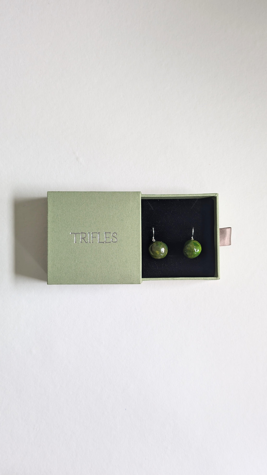 Handmade ceramic orb shaped earrings in olive green with sterling silver ear wires in Trifles gift box.