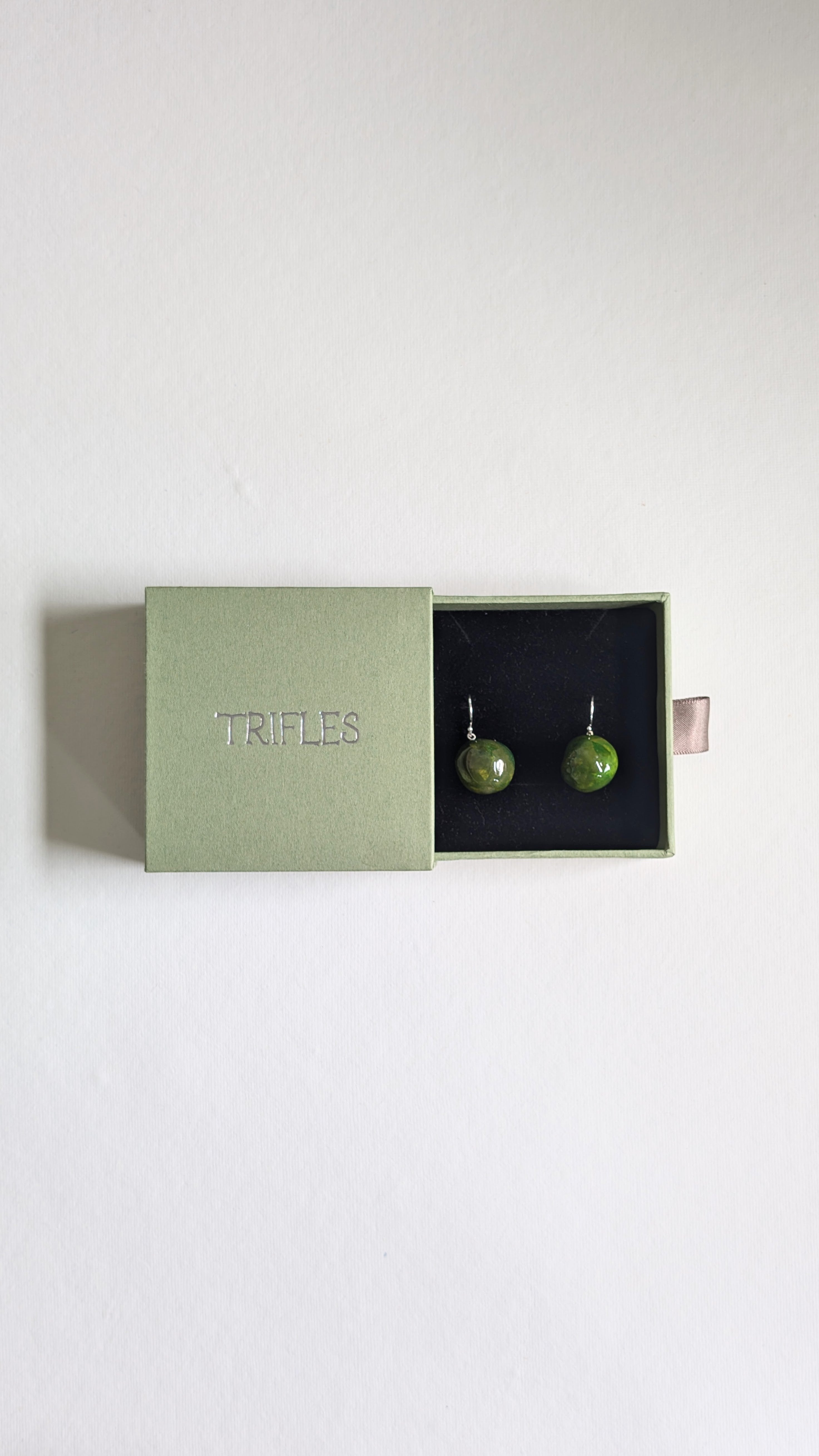 Handmade ceramic orb shaped earrings in olive green with sterling silver ear wires in Trifles gift box.