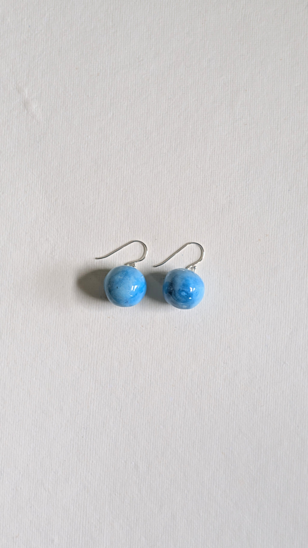 Orb shaped handmade ceramic earrings painted in sky blue and finished with sterling silver ear wires.