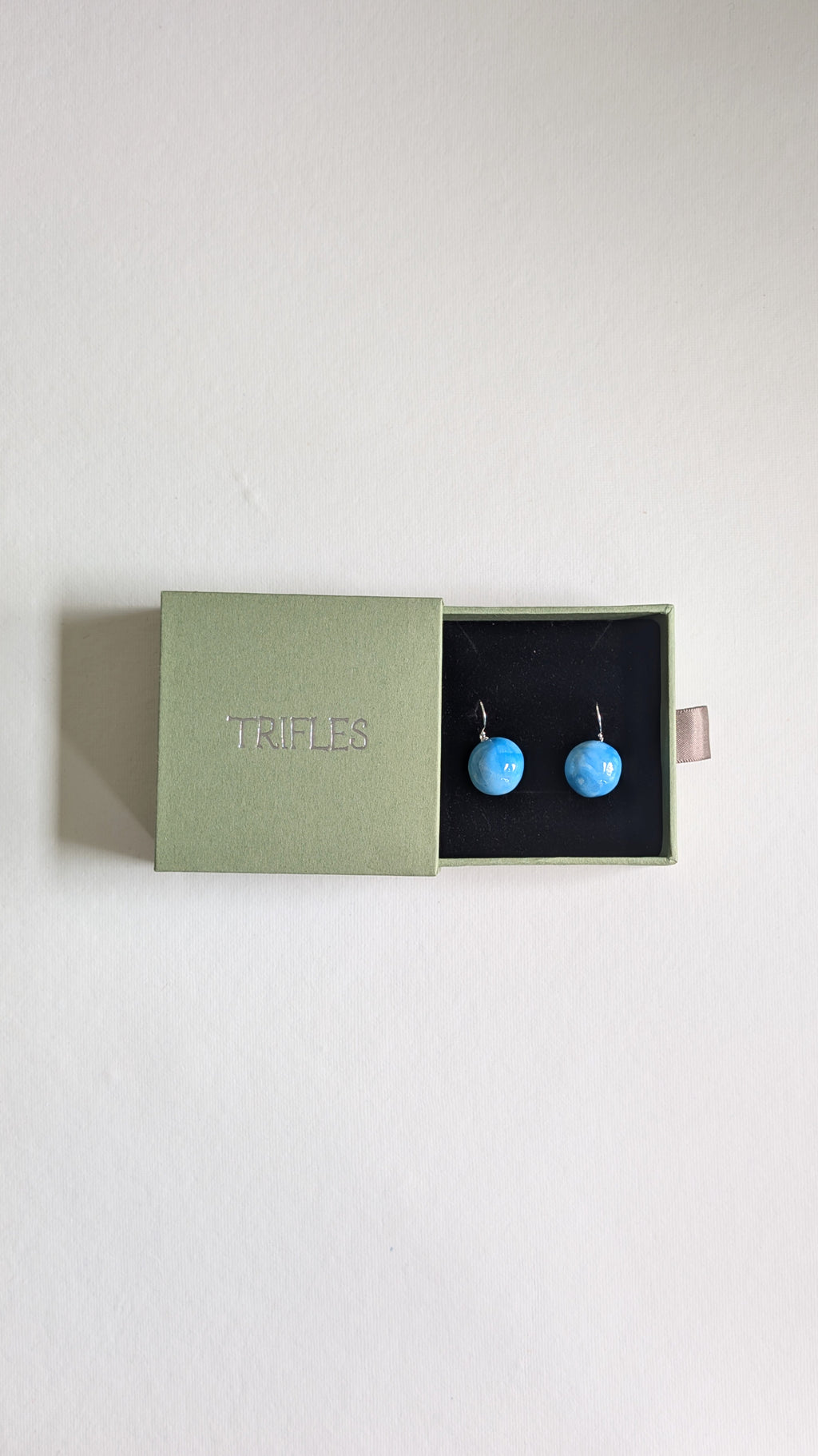Orb shaped handmade ceramic earrings painted in sky blue and finished with sterling silver ear wires in Trifles gift box.