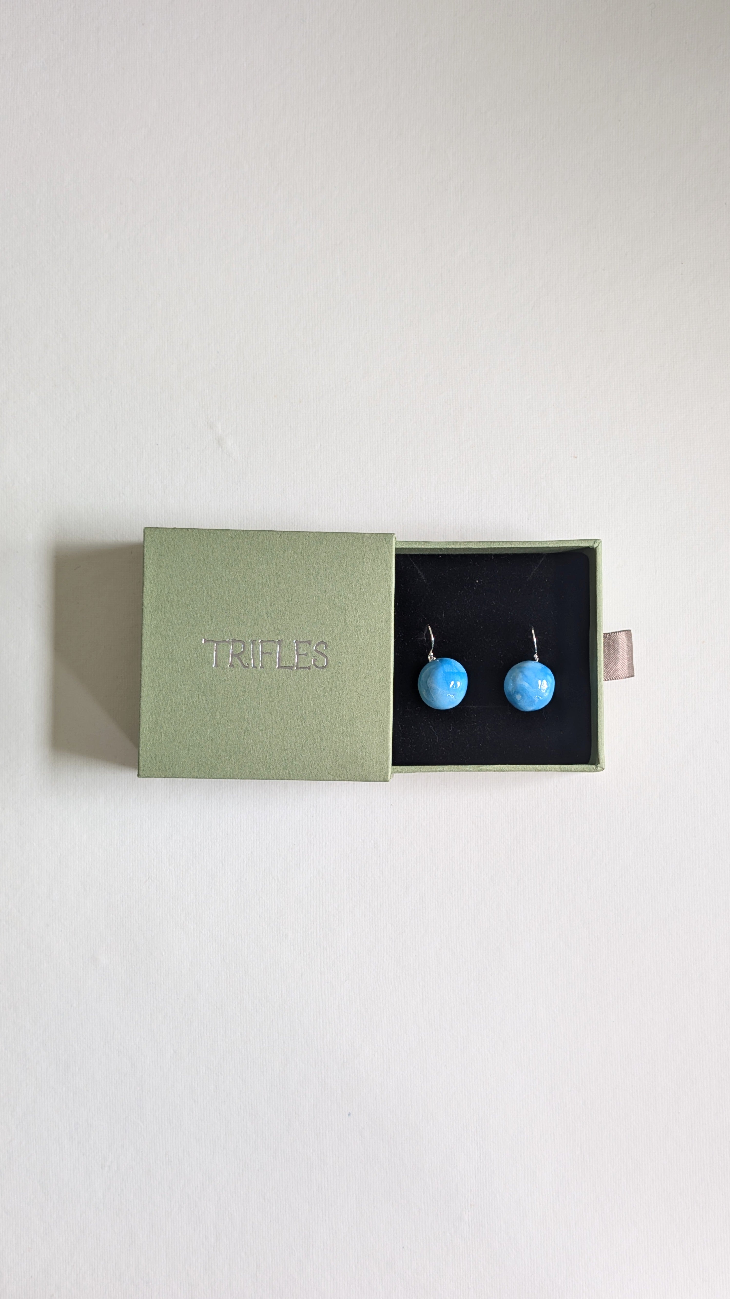 Orb shaped handmade ceramic earrings painted in sky blue and finished with sterling silver ear wires in Trifles gift box.